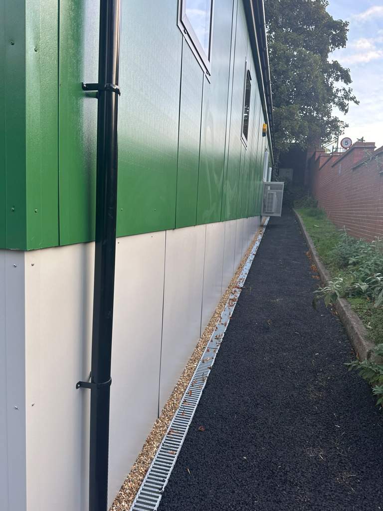 Galvanised channel drain and resurfaced footpath along the building