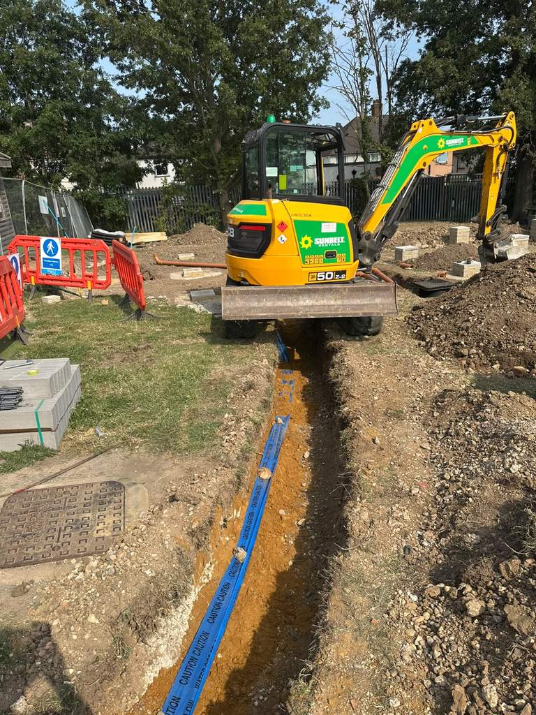 JCB 50Z excavator trenching new water main with marker tape at Hacton