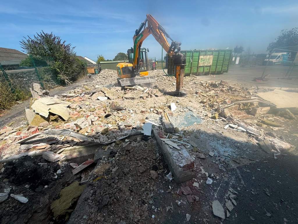 Excavator with hydraulic breaker clearing demolition slab and hardcore