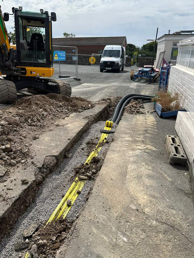 Excavator trenching ducting run with warning tape installed