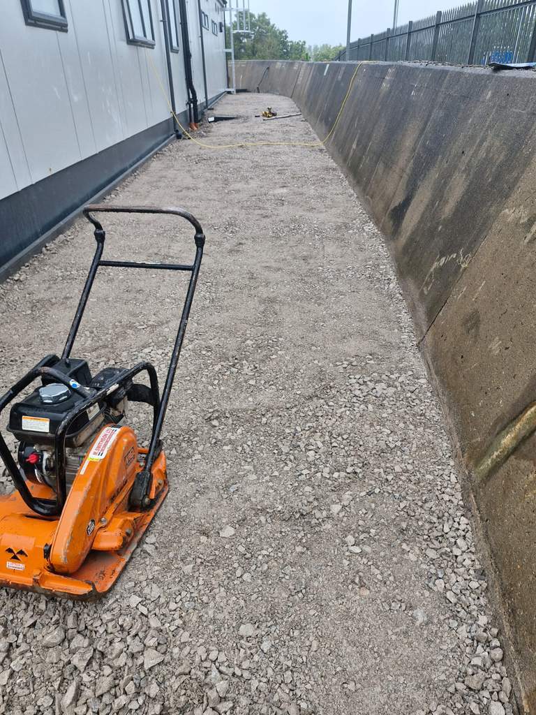Plate compactor on freshly compacted sub-base beside retaining wall