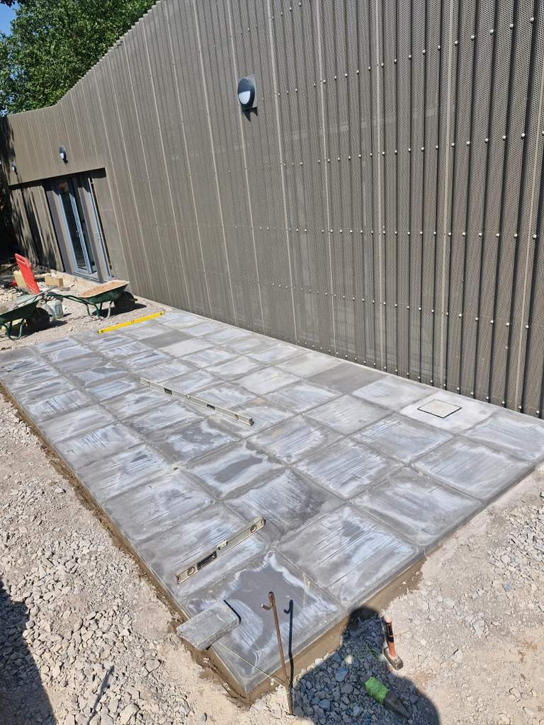 Newly laid concrete flag base alongside clad building elevation