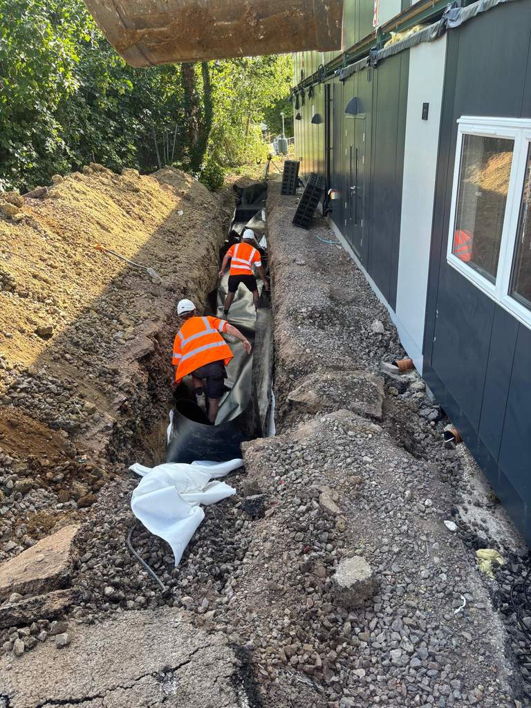 Groundworkers installing membrane-lined attenuation trench