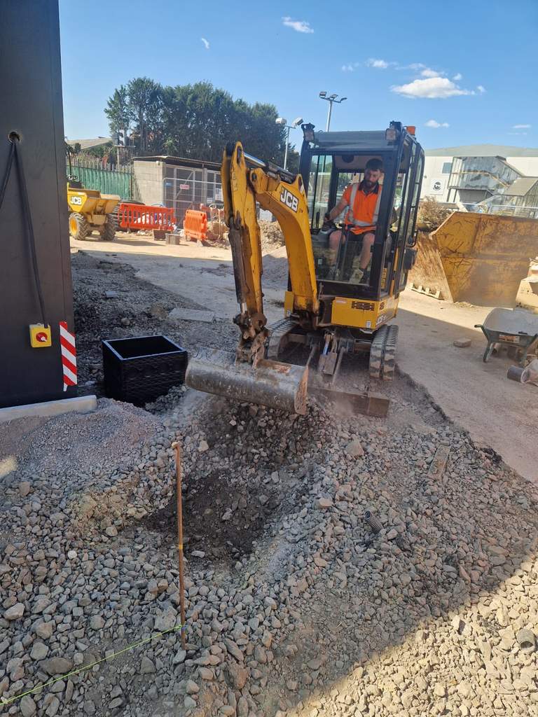 Excavator placing drainage stone around inspection chamber