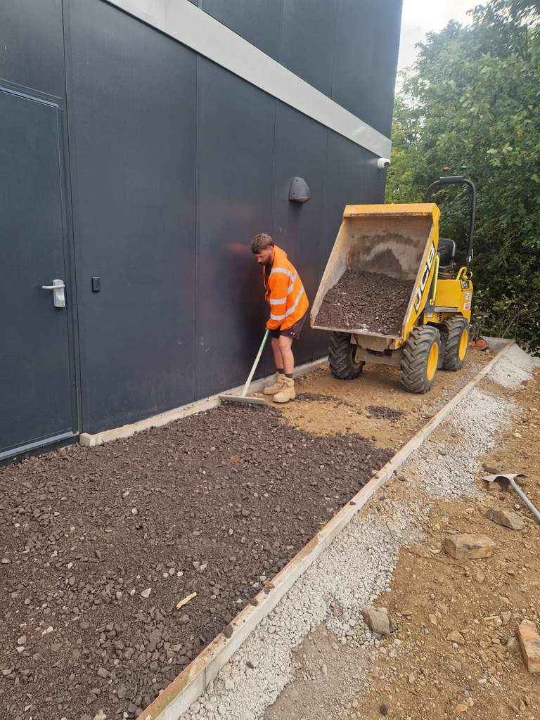 Dumper tipping stone as groundworker rakes kerbed sub-base