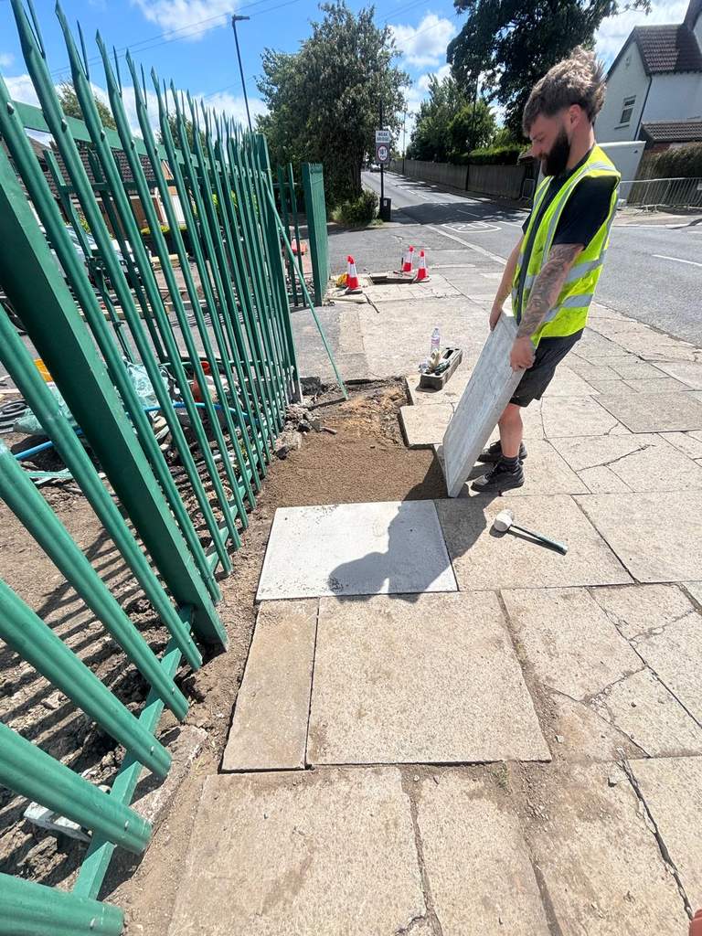 Groundworker laying new concrete paving slabs on footpath